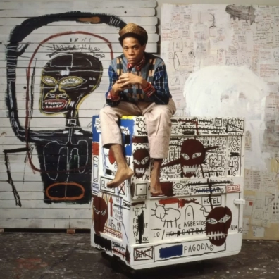 Jean-Michel Basquiat zit op een beschilderde kist in zijn studio, met zijn kunstwerk achter hem. Jean-Michel Basquiat zit op een beschilderde kist in zijn studio, met zijn kunstwerk achter hem.