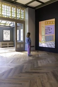 Gallery view with visitor observing Robbie Williams’ large yellow and purple text piece at Moco Museum Amsterdam.