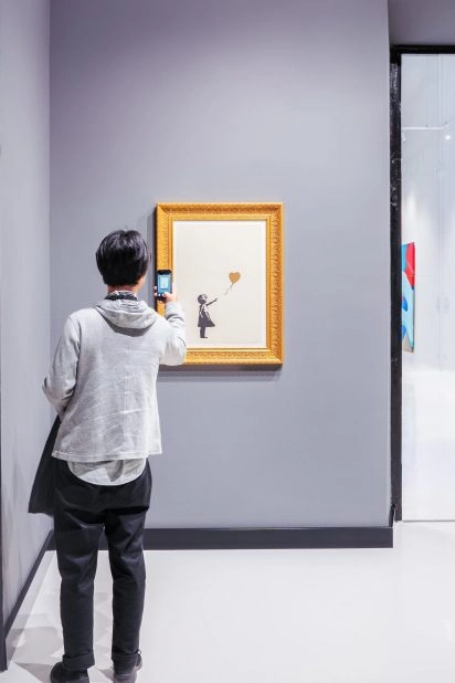 Person photographing Banksy artwork at Moco Museum Barcelona