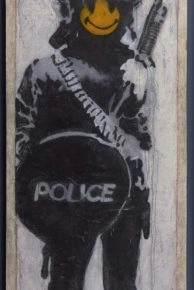 Banksy-kunstwerk van een ME-agent met een gele smiley bij Moco. Banksy-kunstwerk van een ME-agent met een gele smiley bij Moco.