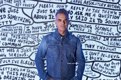 Robbie Williams frente a obra de texto manuscrito en blanco y negro, parte de su exposición en Moco Museum Amsterdam.