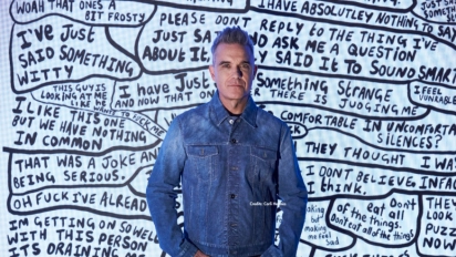 Robbie Williams davanti a un’opera testuale in bianco e nero, parte della sua mostra al Moco Museum Amsterdam.