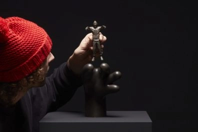 Frankey colocando una pequeña figura de bronce sobre una escultura negra surrealista, parte de Planet Positive Disruption, Moco Museum Amsterdam.