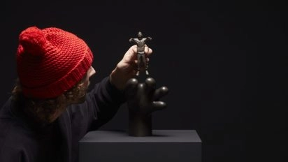 Frankey platziert eine kleine Bronzefigur auf einer surrealen schwarzen Skulptur, Teil von Planet Positive Disruption, Moco Museum Amsterdam.