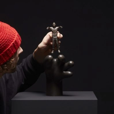 Frankey positioning miniature sculpture on oversized black hand at Moco Museum