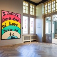 Colorful wall piece by Robbie Williams reading “I Deserve Every Drop of Love You've Got to Give,” shown at Moco Museum Amsterdam.