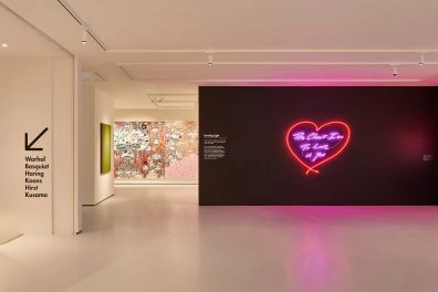Interior of Moco Museum London with neon heart artwork by Tracey Emin on black wall and colorful graffiti in background