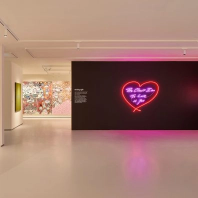 Interior of Moco Museum London with neon heart artwork by Tracey Emin on black wall and colorful graffiti in background