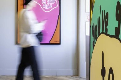 Visitor walking past colorful text-based artwork by Robbie Williams at Moco Museum Amsterdam.