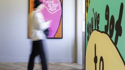 Visitor walking past colorful text-based artwork by Robbie Williams at Moco Museum Amsterdam.